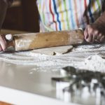Person holding a rolling pin over dough on a kitchen counter