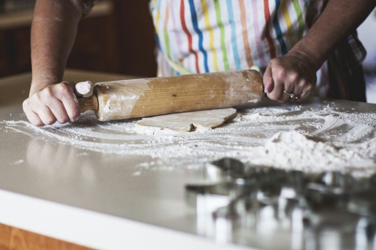 Person holding a rolling pin over dough on a kitchen counter